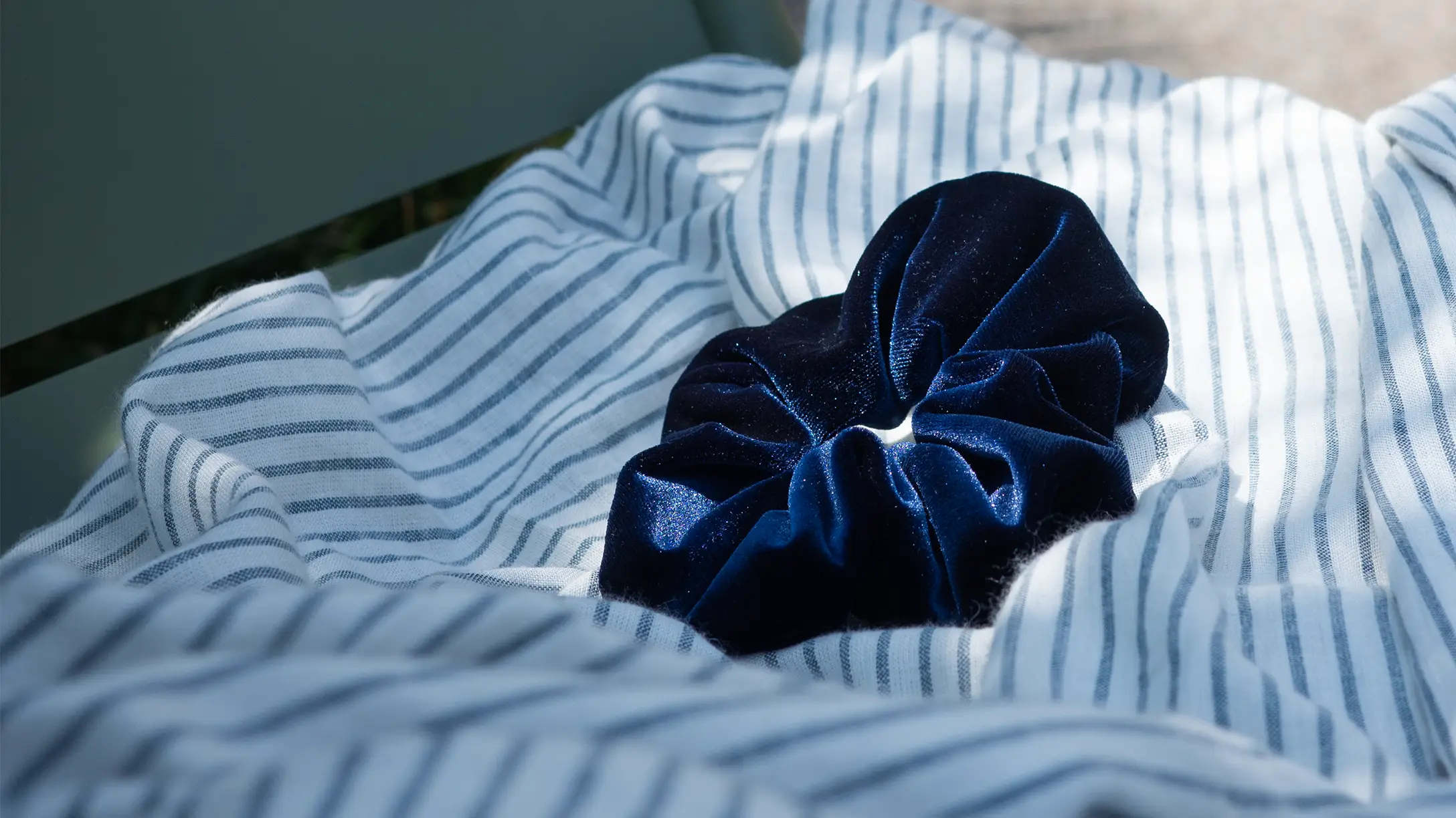 A navy velvet scrunchie resting on striped linen