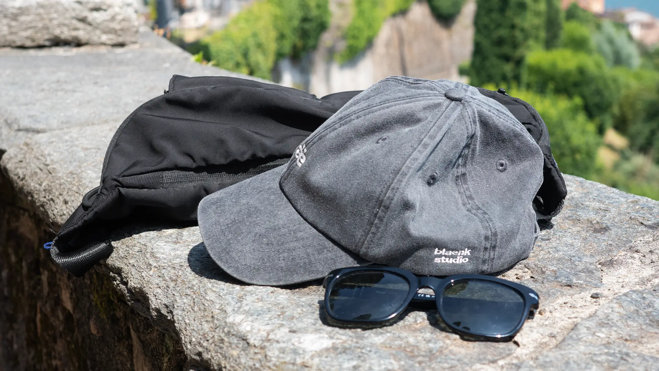 A washed blaenk studio cap and sunglasses on a stone wall
