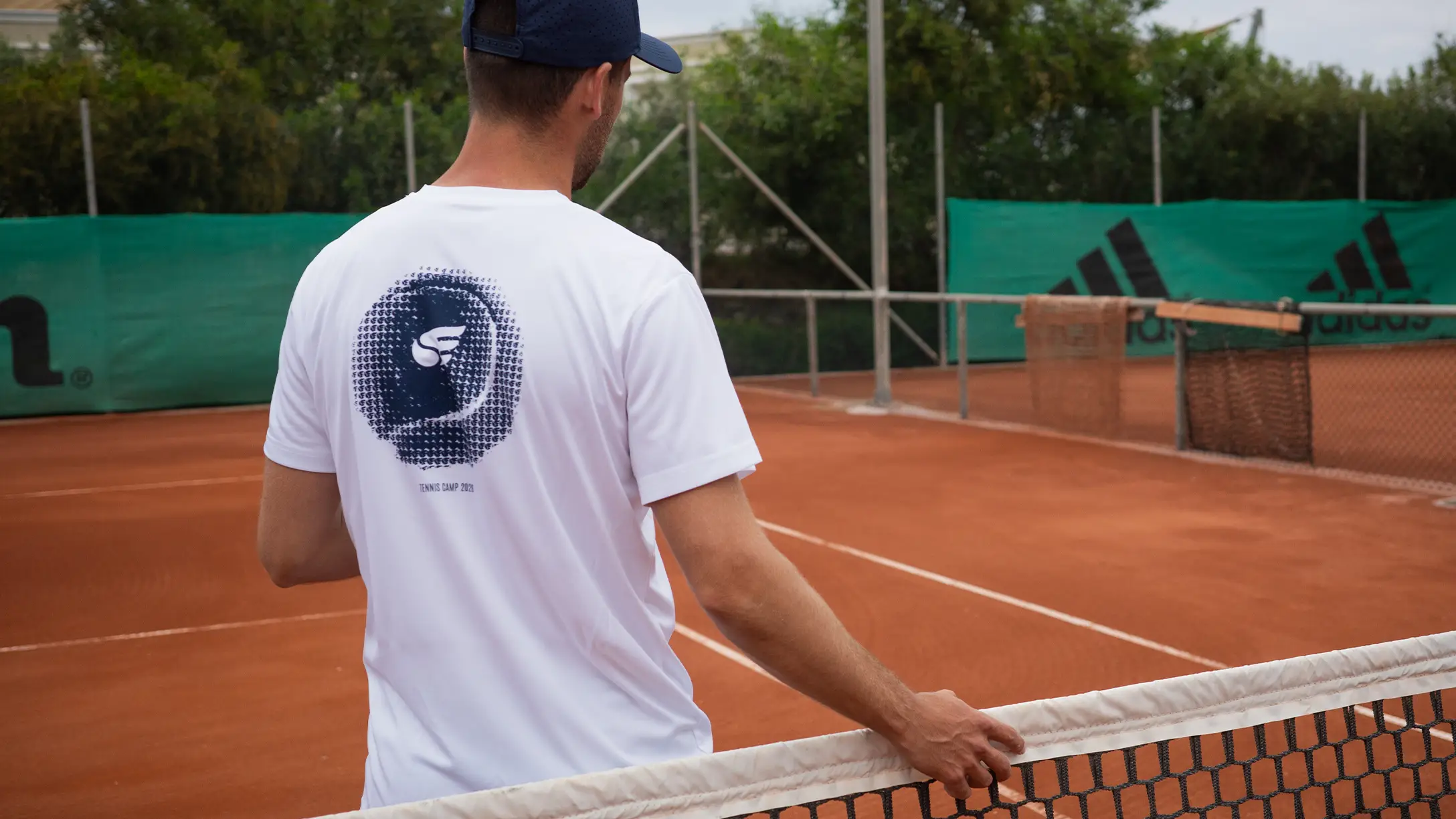 tennis player on a clay court wearing a white club shirt with a subtle logo on the back